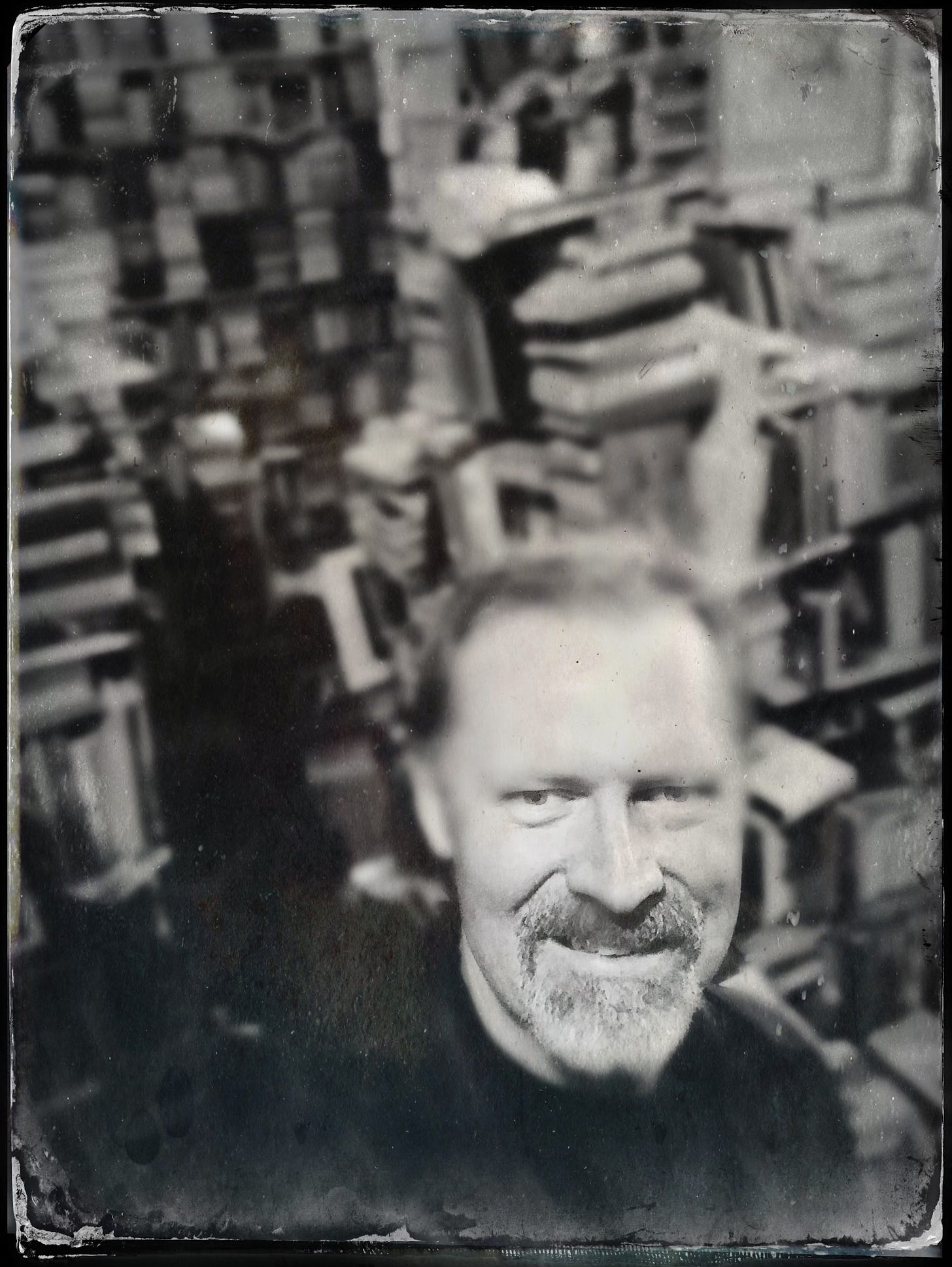 Black-and-white photograph of writer John P. Weiss standing in a narrow aisle of an old bookstore in New Orleans, surrounded by shelves of used books.