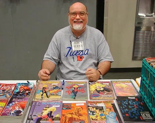 Writer R.A. Jones sits behind a table promoting his various comic-book work. 