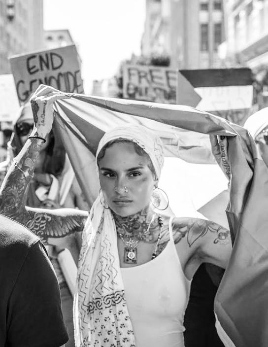 A black and white image of Kehlani holding a flag above their head at a protest.