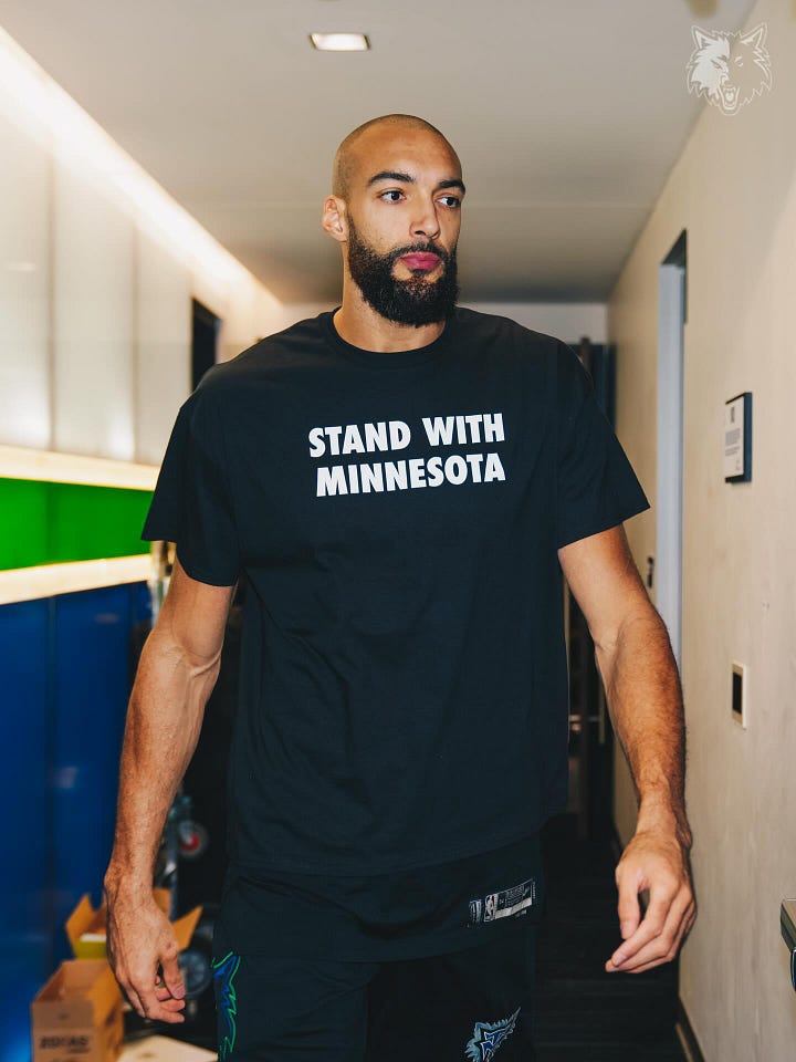 Very tall basketball players wearing black t-shirts that say Stand With Minnesota in white block letters