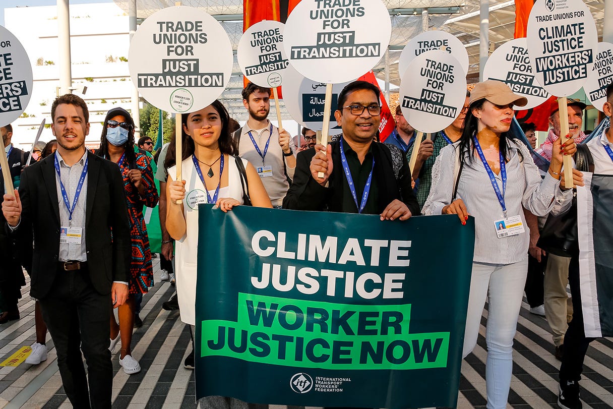 A group of people demonstrating for climate and worker justice. They are holding signs with various slogans, such as ‘Trade unions for just transition’ and ‘Climate justice worker justice now’.