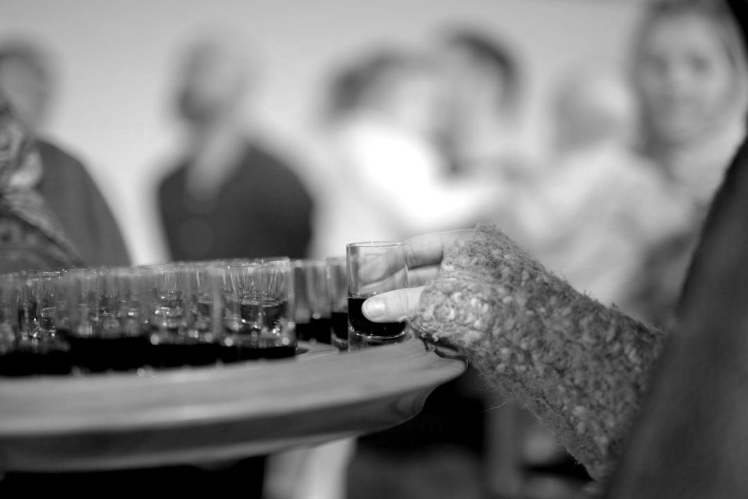 person holding shot glass with red liquid on table top person holding shot glass with red liquid on table top