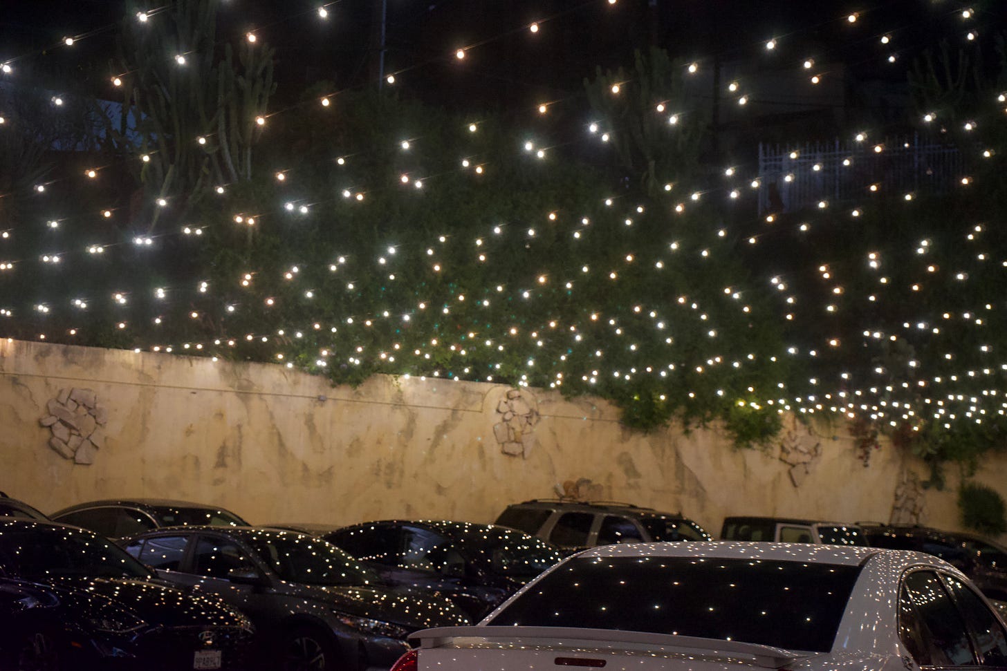 Parking area at night with rows of cars beneath warm string lights hanging overhead against a dark sky. Parking area at night with rows of cars beneath warm string lights hanging overhead against a dark sky.