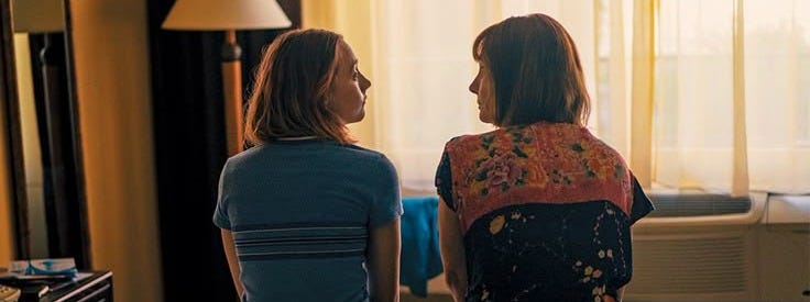 This may contain: two women sitting on the edge of a bed looking at each other in front of a window