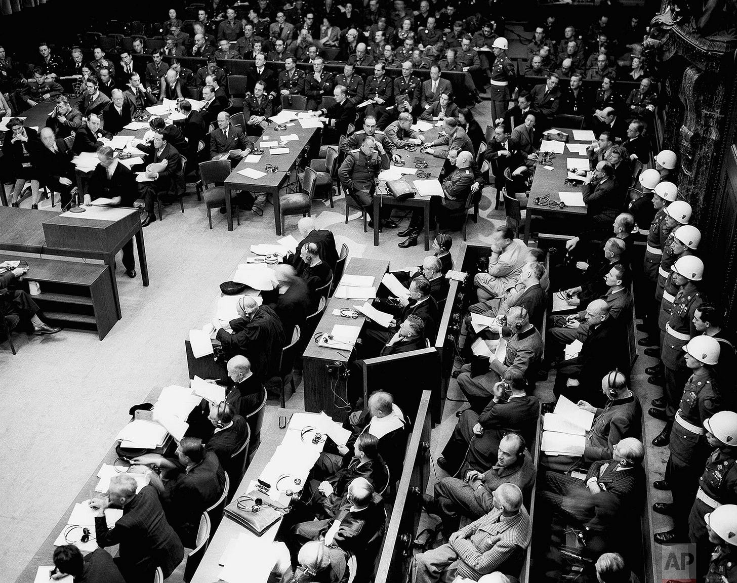 The solemn atmosphere of the Nuremberg courtroom on November 20, 1945, during its inaugural morning session. In the foreground, left, the defendants are seated, flanked by watchful guards and their legal counsel, as history unfolds. The solemn atmosphere of the Nuremberg courtroom on November 20, 1945, during its inaugural morning session. In the foreground, left, the defendants are seated, flanked by watchful guards and their legal counsel, as history unfolds.