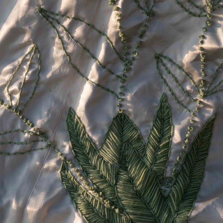 Large leafed green plant growing at the base of a tree next to a detailed image of embroidered stitches of that same large leafed green plant.