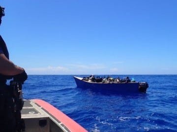 An armed US Coast Guardsman keeps a watchful eye over a human smuggling vessel as they approach to board and commandeer the boat. An armed US Coast Guardsman keeps a watchful eye over a human smuggling vessel as they approach to board and commandeer the boat.