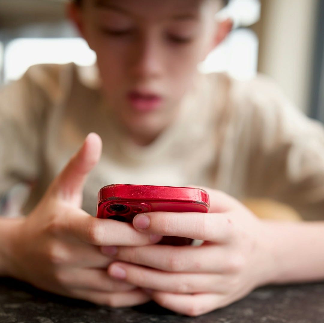A boy focuses on his red cellphone