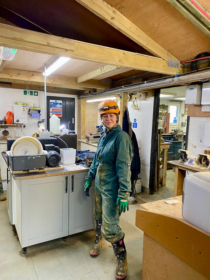 Two photos side by side. On the left, a woman stands beside an e-bike outside stone cottages in a Peak District village, smiling and giving a thumbs up. On the right, the same woman wears protective clothing and a helmet inside a workshop, standing next to machinery while making jewellery.