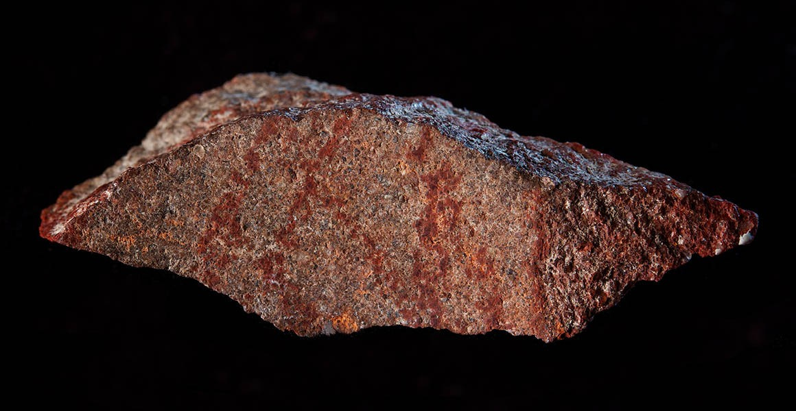A pointed red stone with darker lines acorss it in a hash pattern