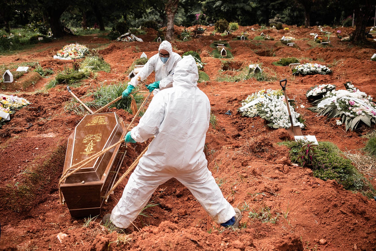 Coveiros com equipamentos de proteção enterram caixão em cova aberta no Cemitério Vila Alpina, em São Paulo, durante pandemia de COVID-19. Coveiros com equipamentos de proteção enterram caixão em cova aberta no Cemitério Vila Alpina, em São Paulo, durante pandemia de COVID-19.