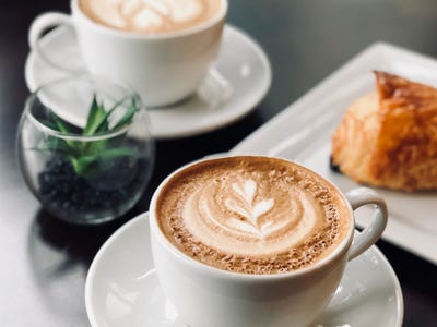 Two coffee cups on a table with a pastry