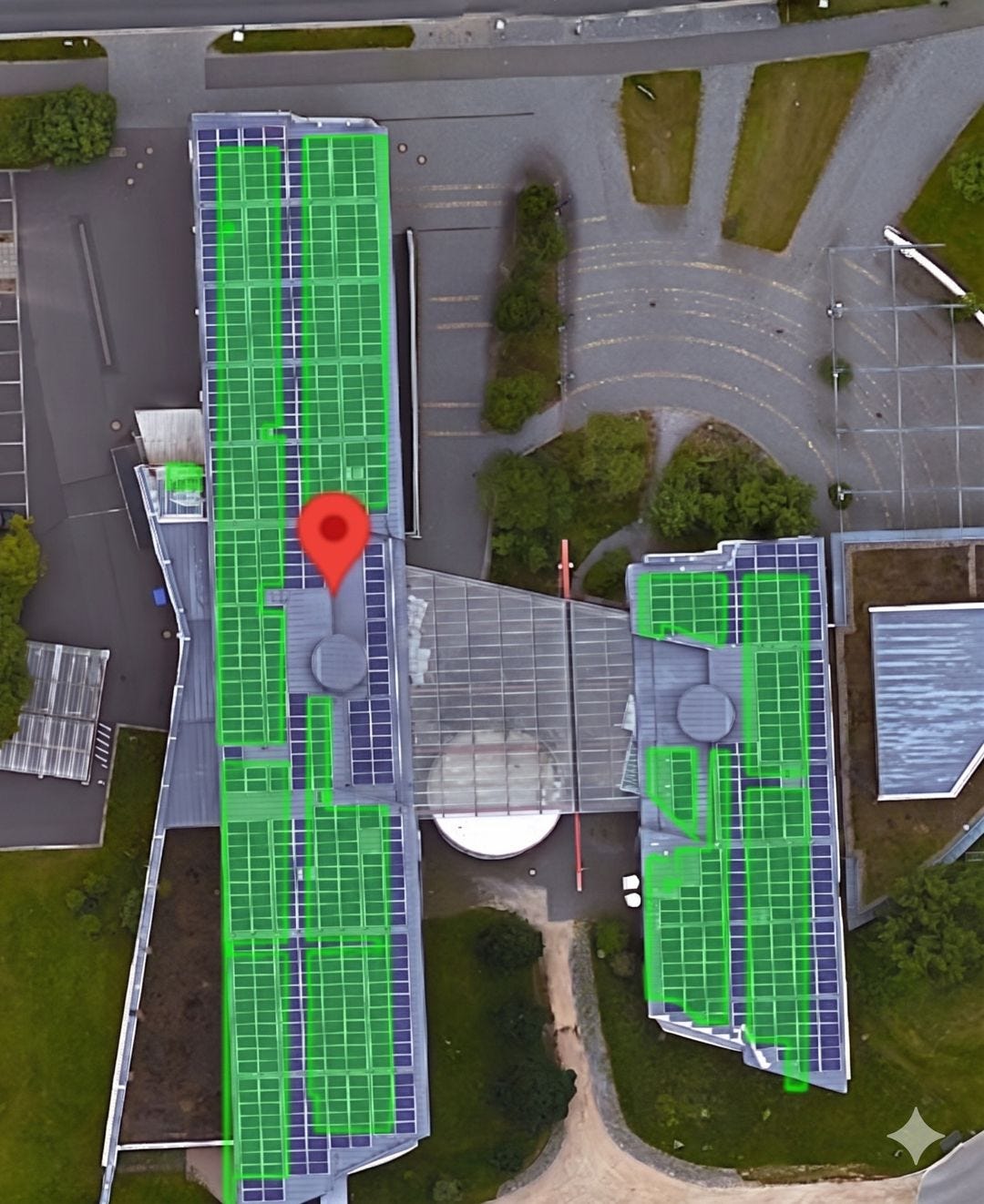 An overhead aerial view of a building complex features extensive solar panel installations across its various roof levels. Semi-transparent green rectangles highlight sections of the solar arrays, and a large red map pin marks a central location on the main building's roof. An overhead aerial view of a building complex features extensive solar panel installations across its various roof levels. Semi-transparent green rectangles highlight sections of the solar arrays, and a large red map pin marks a central location on the main building's roof.