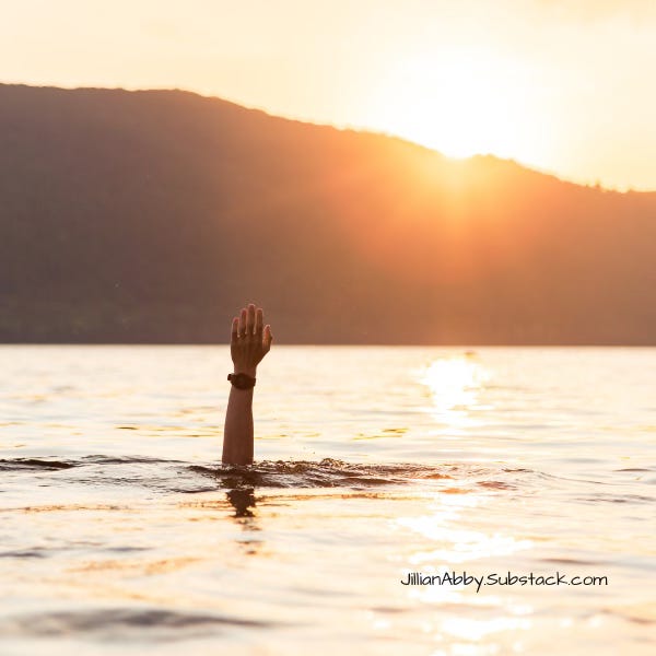 A single hand is raised out of a calm body of water at sunset, as if reaching for help or signaling distress. The sun sets behind a dark silhouette of a mountain, casting a golden glow across the water. The atmosphere is serene yet evokes a strong emotional contrast between beauty and struggle. In the bottom right corner, the text reads: “JillianAbby.Substack.com”.