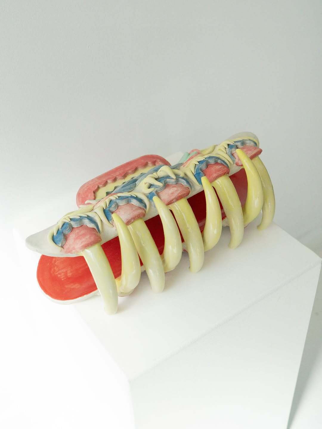 Ceramic Hair Clip Monster by Eri Maeda, a large sculptural hair clip with pastel layers and sharp yellow claw like teeth, displayed on a white plinth. Contemporary ceramic sculpture, 2025.