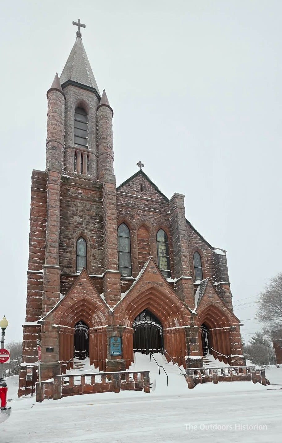 The towering red sandstone facade and twin steeples of the historic St. Anne's Church in Calumet, Michigan. The architecture is a prominent landmark of the Copper Country's immigrant history.