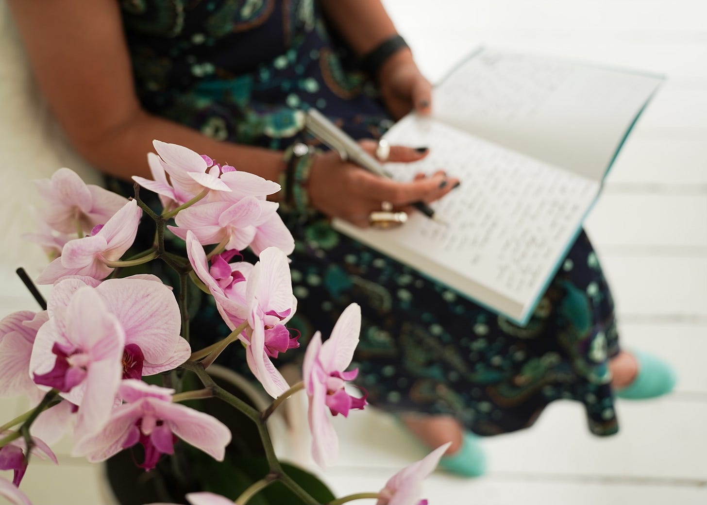 A close up of Sanjida writing in her notebook with pink orchids in the foreground