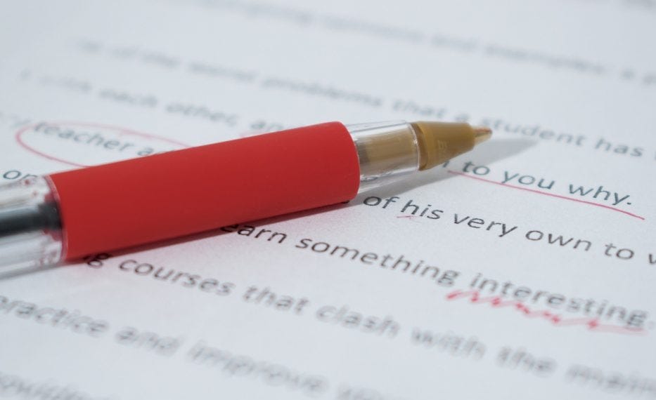 A red sheathed writing pen laying on top of white paper with typing on it. Some words are crossed out with red ink. A red sheathed writing pen laying on top of white paper with typing on it. Some words are crossed out with red ink.