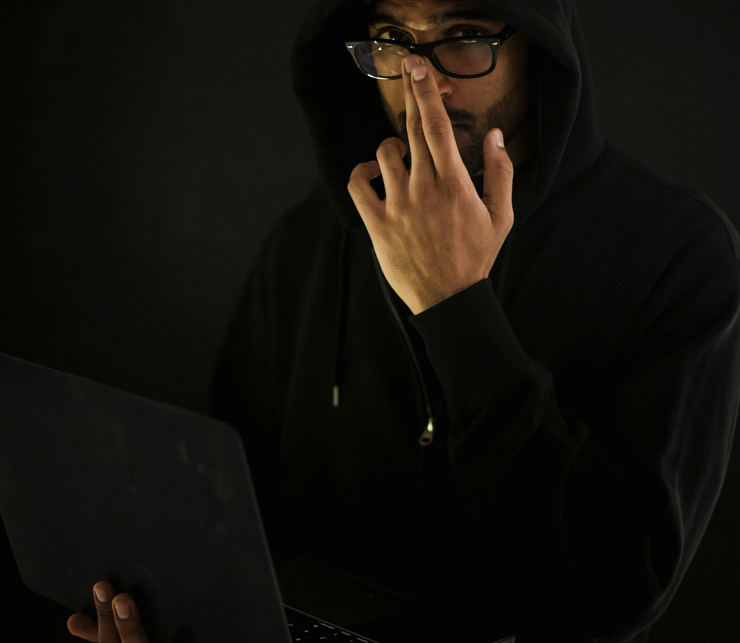 A male computer geek with glasses in eyeglasses with laptop in darkness
