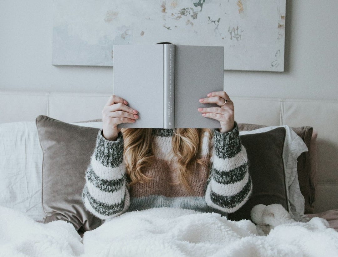 woman sitting on bed while holding book