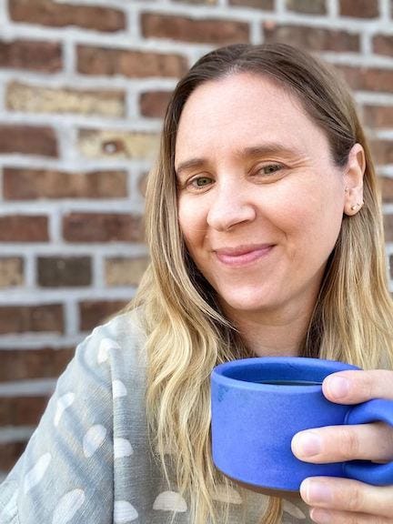 Blonde woman holding blue coffee cup, smiling