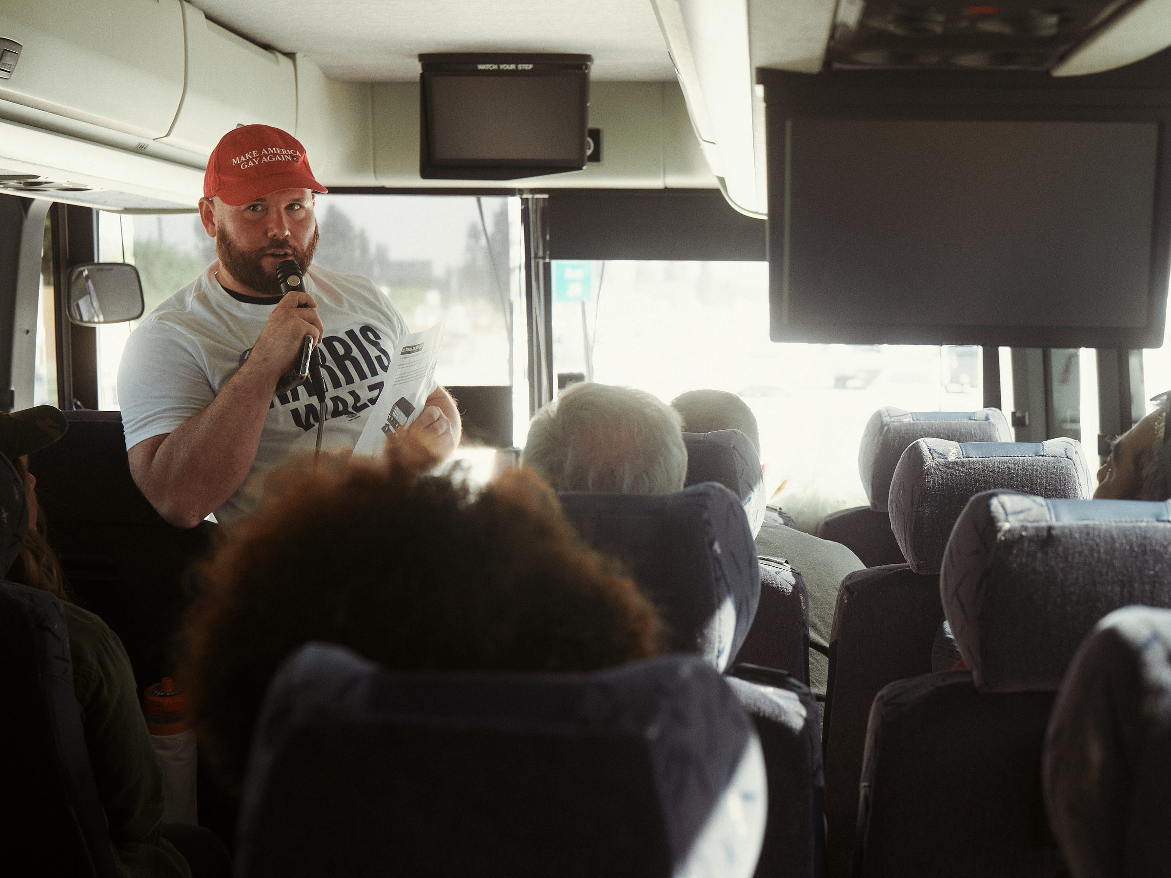 Man wearing a Harris Walz campaign t-shirt talks on the microphone to the bus riders, photographed by Los Angeles photographer Afonso Salcedo.