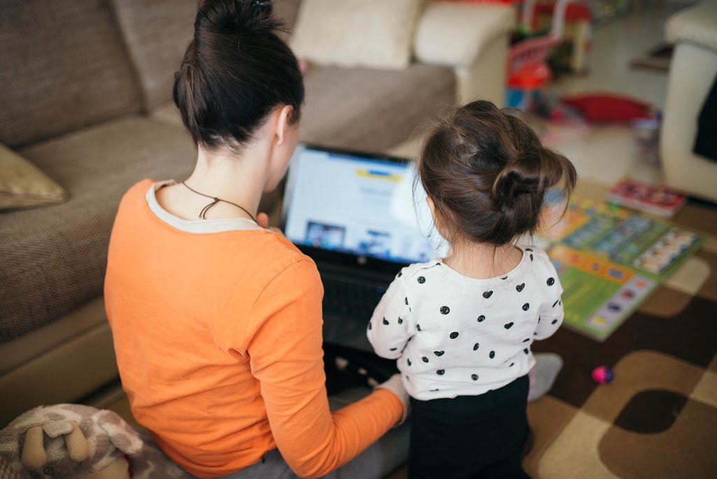 Mom teaches daughter for work on laptop.