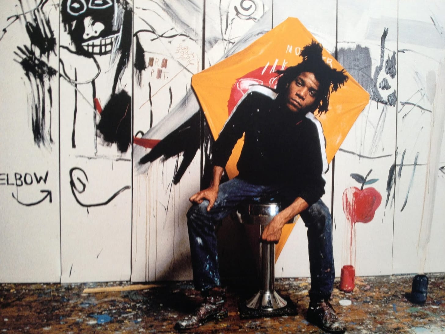 jean michele basquiat sitting in front of his paintings against a white backdrop.
