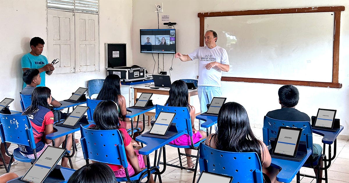 Professor em sala de aula junto a crianças que acompanham as atividades com uso de tablets Professor em sala de aula junto a crianças que acompanham as atividades com uso de tablets