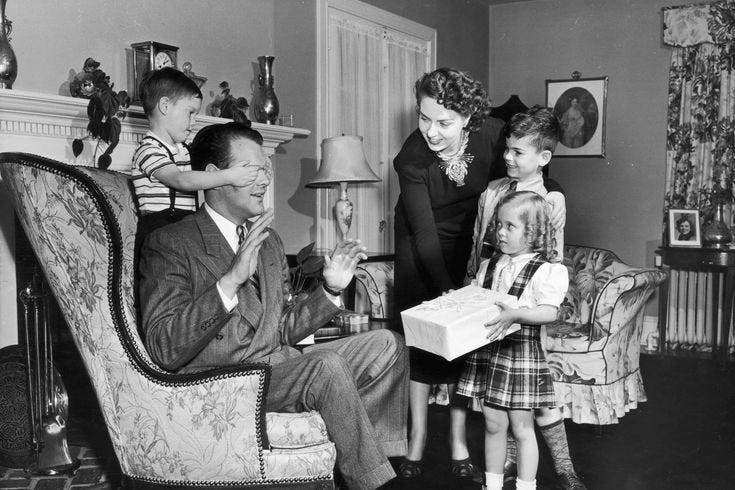 This may contain: an old black and white photo of a family in their living room with the child holding a box