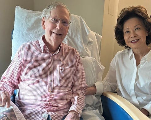 a man sits in a hospital bed with his wife holding a newspaper a man sits in a hospital bed with his wife holding a newspaper