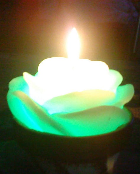 Three flower-shaped candles, glowing in, orange, green, and purple, respectively.