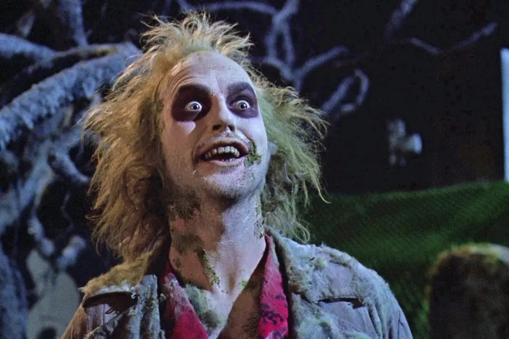 Michael Keaton as Beetlejuice; head and shoulders, white face make up dark eyes wild blonde hair