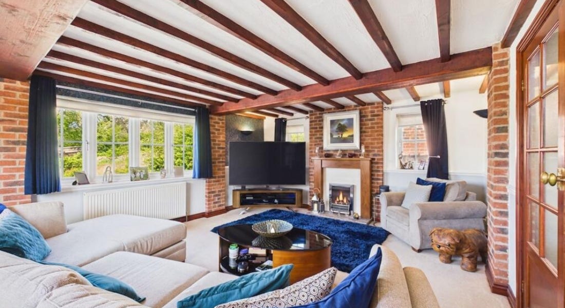 A living room with wooden beams, a white sofa with blue cushions, a TV, and windows
