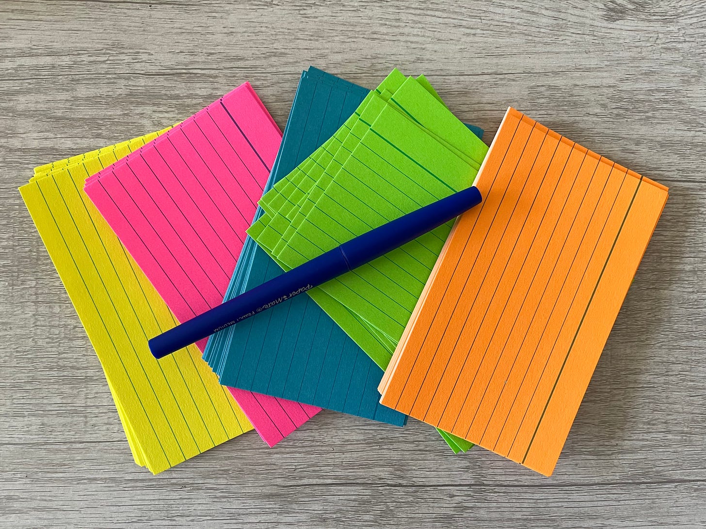 Neon colored index cards and a blue pen on a wood desk