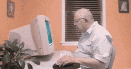 an elderly man is sitting at a desk in front of a computer monitor .