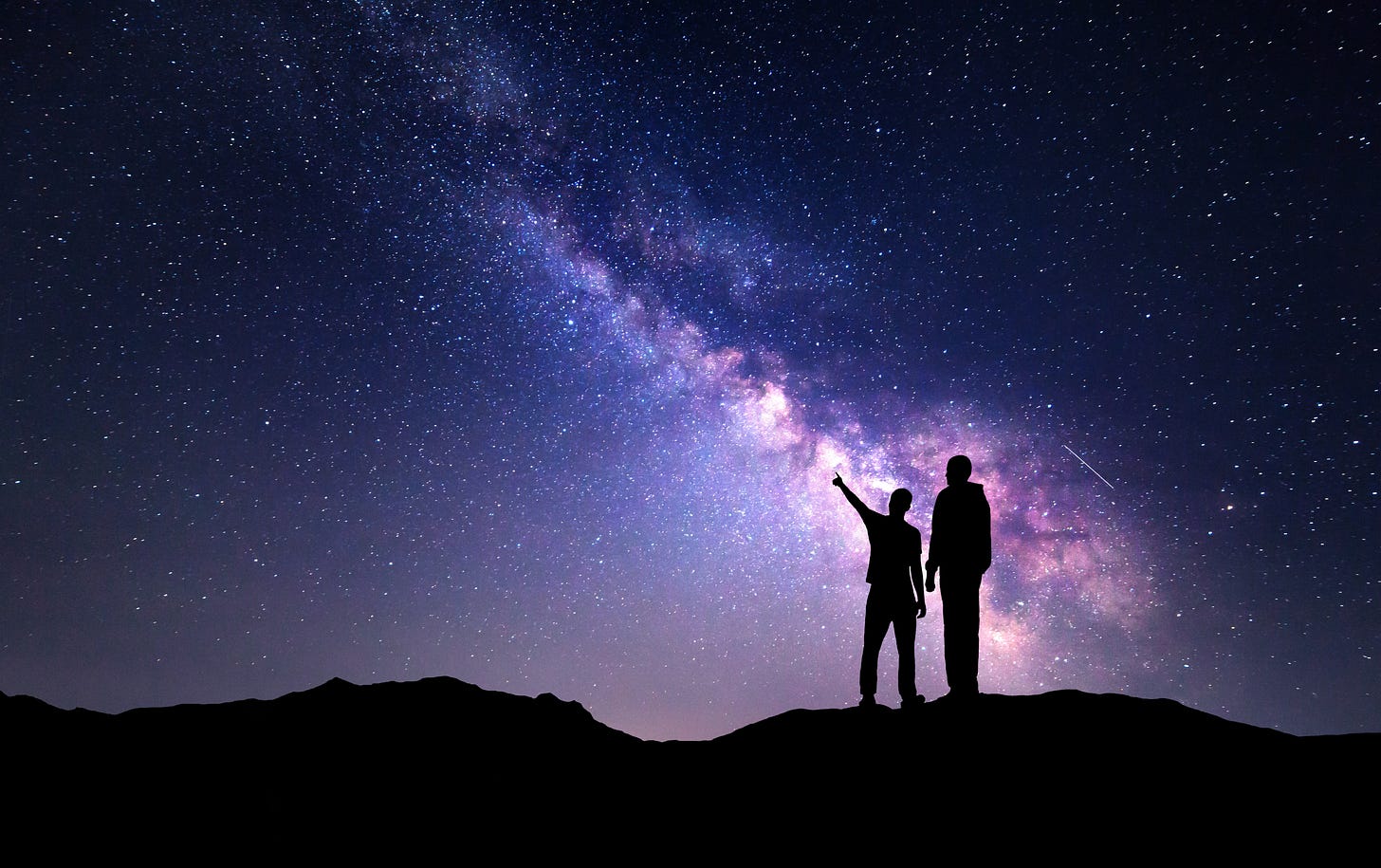 Two people silhouetted against a night sky gazing at the Milky Way Two people silhouetted against a night sky gazing at the Milky Way