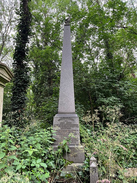 Three obelisk grave monuments with adornments. One has a hand pointing upwards on top, one a laurel wreath carved into the front, and one has an urn on top.