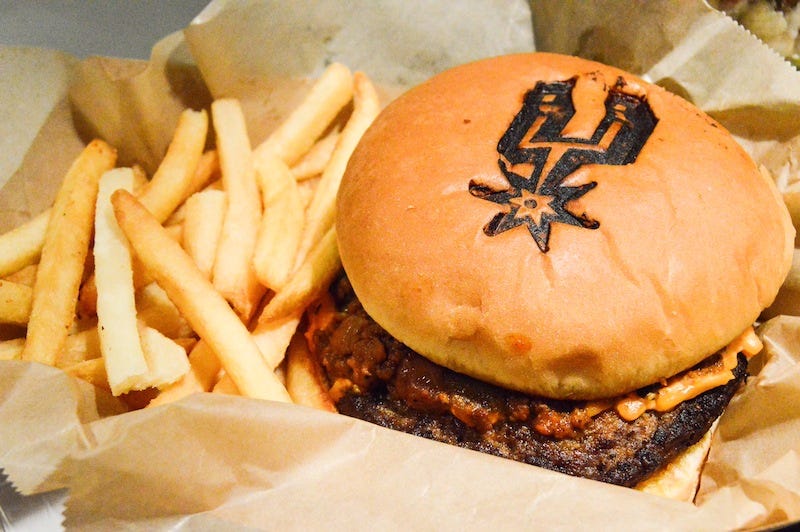 Usher John Moreno waits by a new mural, "Light It Up," by artist Elizabeth Carrington, to direct Spurs fans in the right direction. Photo by Lea Thompson. 2. Fans can stop by the Charter Level for the"Spurburger," a Spurs-inspired burger topped with roasted poblanos, pimento cheese and classic chili. Photo by Lea Thompson.
