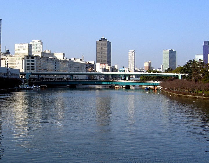 Two pictures of Tenmabashi, one from the Edo era, and one from the early twenty-first century. The Edo era bridge curves across the water on tall pillars of wood, while the modern bridge goes flat across the river and is made of metal and concrete.