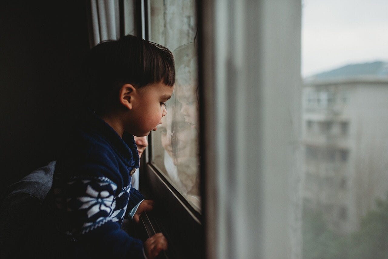 father and son looking out of a window from a high-rise building in wuhan china during initial covid outbreak with the son wanting to go downstairs to play. A moment documented by phoenix family photographer Amy Dangerfield.