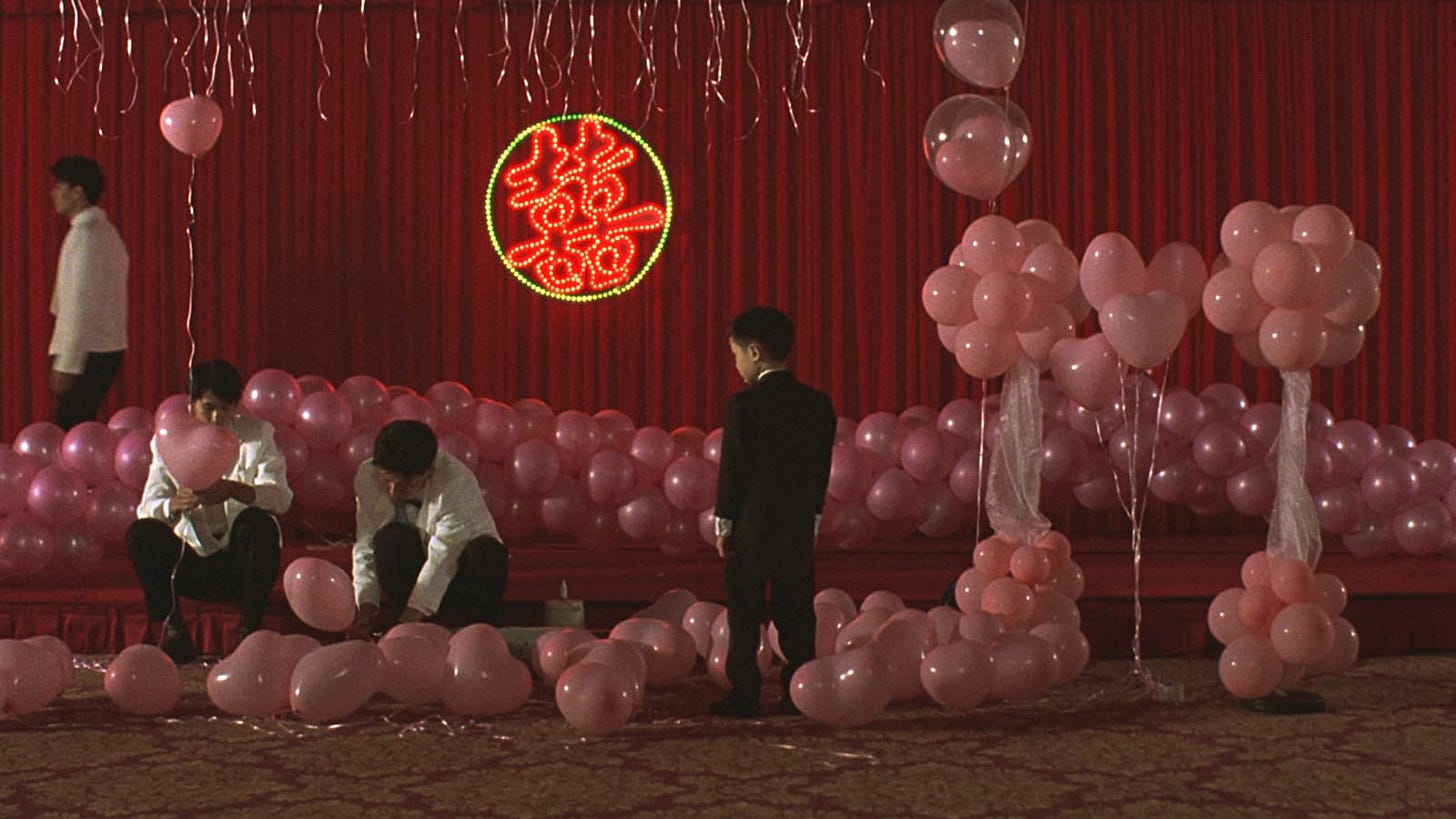 Yi Yi | Still features a Yang-Yang with his back turned behind the camera, observing pink heart balloons being set up for a ceremony.