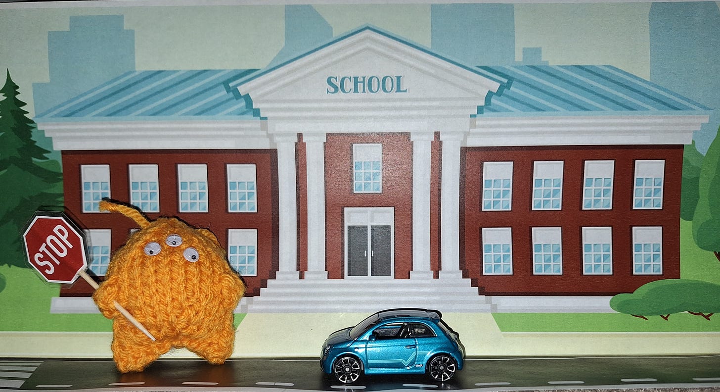 a knitted alien holding a stop sign in front of a school and a toy car.