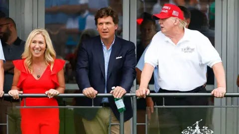 Icon Sportswire via Getty Images Marjorie Taylor Greene, smiling in a red dress, Tucker Carlson in a suit coat and khaki pants, and Donald Trump in a white gold shirt and a red MAGA baseball cap stand side by side leaning on a railing Icon Sportswire via Getty Images Marjorie Taylor Greene, smiling in a red dress, Tucker Carlson in a suit coat and khaki pants, and Donald Trump in a white gold shirt and a red MAGA baseball cap stand side by side leaning on a railing