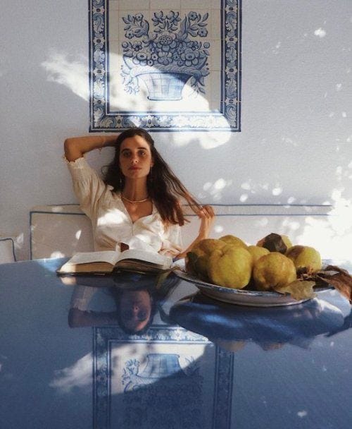 This may contain: a woman is sitting at a table with fruit on it and an open book in front of her