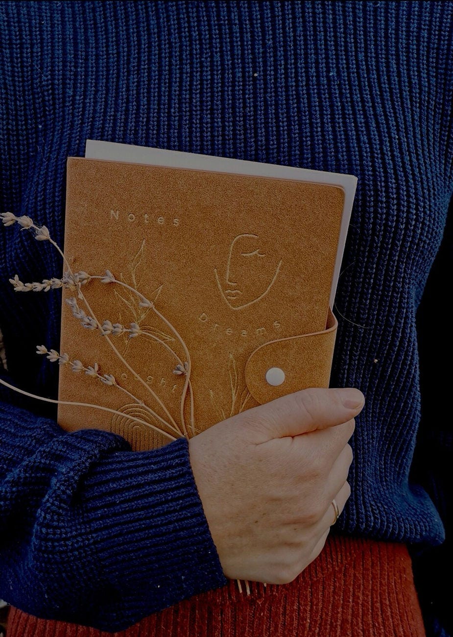 Woman in navy blue jumper holding brown notebook with some lavander.