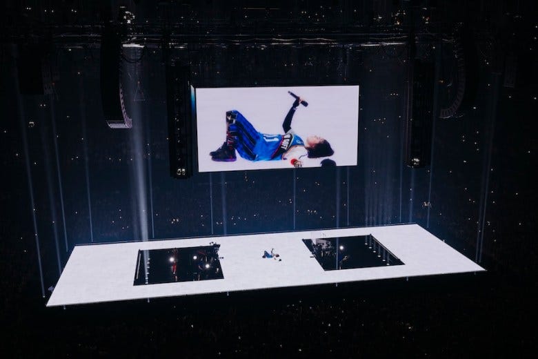 At her tour for the album, "Hit Me Hard and Soft," Billie Eilish lies on the middle of a stage. A screen is above her, projecting her to the crowd. 