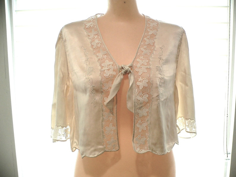May include: A white satin top with lace trim and a tie at the neckline.