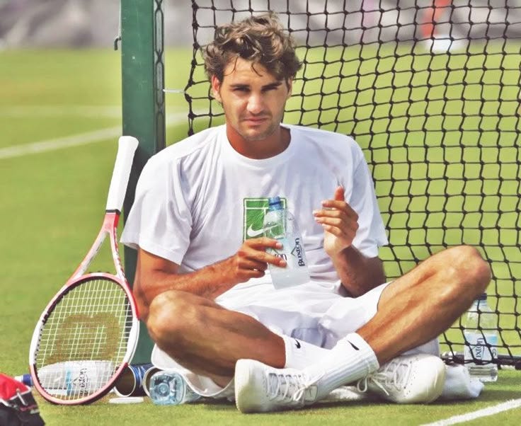 This may contain: a man sitting on the ground holding a drink and tennis racket in his hand This may contain: a man sitting on the ground holding a drink and tennis racket in his hand