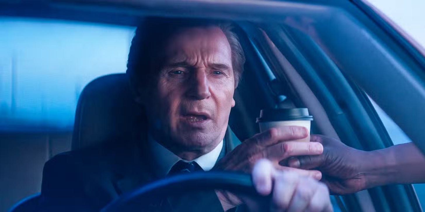 Liam Neeson as Drebin behind car wheel, reaching for a cup of coffee handed into car by disembodied hand
